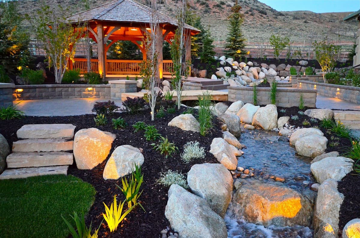 Custom landscape design with boulder water feature, gazebo, and low-voltage lighting in Lake Orion MI