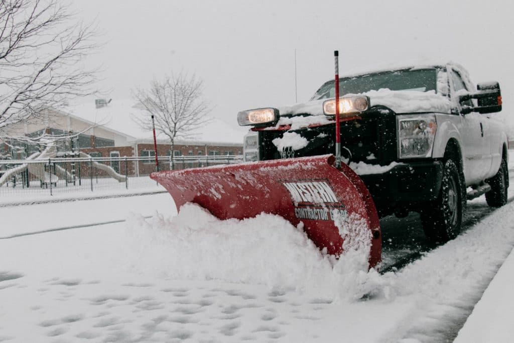 Red snow plow truck clearing a commercial parking lot during heavy snowfall in Lake Orion Michigan
